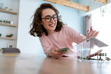 Happy Woman Saving Money In Piggy Bank At Home
