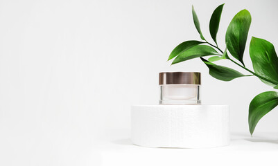 a mock up white jar of cream on a white gray background, on a white table with green leaves of a tro