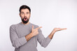 © Tetiana - Photo of young man amazed shock omg point finger product offer select isolated over grey color background