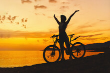 Silhouette Of Active One Free Happy Joyful Carefree Inspired Woman Bicycler With Open Arms Standing Alone With Bicycle Outdoors Against Sunset Sky