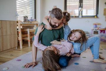 Wall Mural - Cheerful father with three little daughters playing together at home.