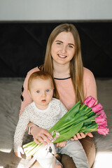 Wall Mural - Mother's day concept. Cute little boy greeting mother with a bouquet of flowers tulips at home. Mom and son smiling and hugging. Happy family holiday and togetherness.