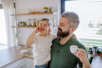 Wall Mural - Father holding his little daughter when drinking coffee at home.