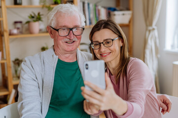 Wall Mural - Adult daughter visiting her senior father at home and taking selfie.