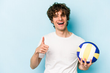 Young caucasian man playing volleyball isolated on blue background smiling and raising thumb up