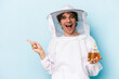 Young caucasian beekeeper man isolated on blue background smiling and pointing aside, showing something at blank space.