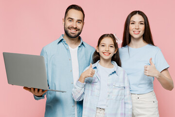 Wall Mural - Young happy fun parents mom dad with child kid daughter teen girl in blue clothes hold use work on laptop pc computer show thumb up isolated on plain pastel light pink background. Family day concept.