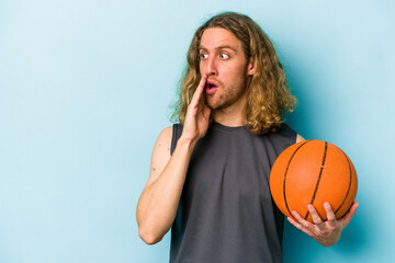 Wall Mural - Young caucasian man playing basketball isolated on blue background is saying a secret hot braking news and looking aside