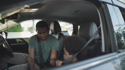 Wall Mural - African American Father is fastening seat belt for his boy in the car before travel, Road trip, Car safety concept.