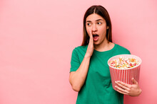 Young Caucasian Woman Holding Popcorn Isolated On Pink Background Is Saying A Secret Hot Braking News And Looking Aside