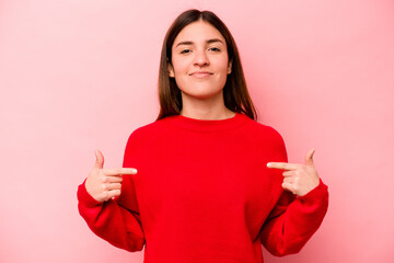 Wall Mural - Young caucasian woman isolated on pink background person pointing by hand to a shirt copy space, proud and confident