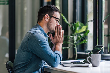 Thoughtful businessman working on laptop while sitting at table in home office