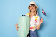 Young Happy Woman Wearing Straw Hat Holding British Flag Over Isolated Blue Background In Vacation With Travel Suitcase