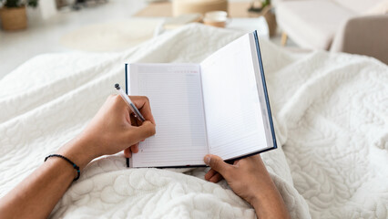 Canvas Print - Male Holding Planner In Hands Taking Notes In Bedroom, POV