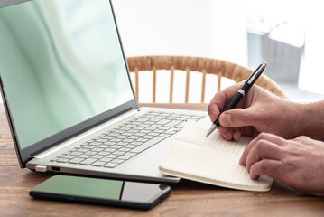 Wall Mural - man taking notes on paper while using laptop computer, e-learning or working from home concept