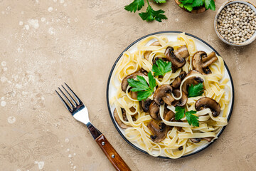 Cooked pasta with mushrooms with parsley on plate on beige stone kitchen table background, top view. Vegan cooking and eating, italian cuisine recipe