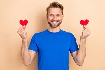 Sticker - Photo of young cheerful guy hold little paper heart shape romantic cardiac isolated over beige color background