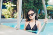 A petite Filipina woman in a black bikini top and wearing dark shades by the poolside. Summer vacation concept.