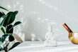 Decorative white Buddha statuette, green plant and tibetian singing bowl on the white background with sun light shadows. Meditation and relaxation ritual. Exotic massage. Minimalism. Copy space.