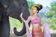 © somchairakin - Asian Woman with traditional thai dress look at her cute elephant, relationship between people and animals.