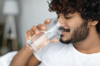 © Prostock-studio - Happy curly young man taking glass of water in bed