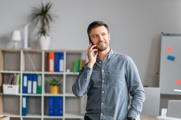 Aufkleber - Positive mature man in office talking on mobile phone near workplace, having conversation with client