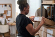© AnnaStills - Young black woman checking address of receiver on packed cardboard box while working with parcels in warehouse against colleague