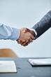 © Seventyfour - Vertical close up of two business people shaking hands at meeting against simple blue background