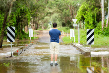 Young Man Looking At Floodwaters Over Causeway On Country Road