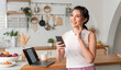 © NaMong Productions - Young woman Asian happy and interested in thinking using mobile phone in kitchen room.