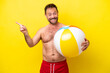 Middle age caucasian man holding beach ball isolated on yellow background pointing finger to the side
