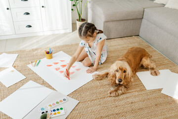 Wall Mural - A girl draws hearts for his mother sitting on carpet floor in living room, cocker spaniel dog lying nearby