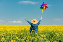 Woman In Hat With Pinwheel In Rapeseed Field
