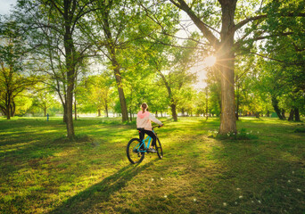 Wall Mural - woman riding a mountain bike near green trees at sunset in spring. colorful landscape with sporty gi