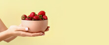Hands Of Woman Holding Bowl Of Ripe Strawberry On Light Yellow Background With Space For Text