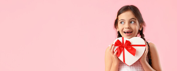 Wall Mural - Funny little girl holding heart-shaped gift box on pink background with space for text. Valentine's Day celebration