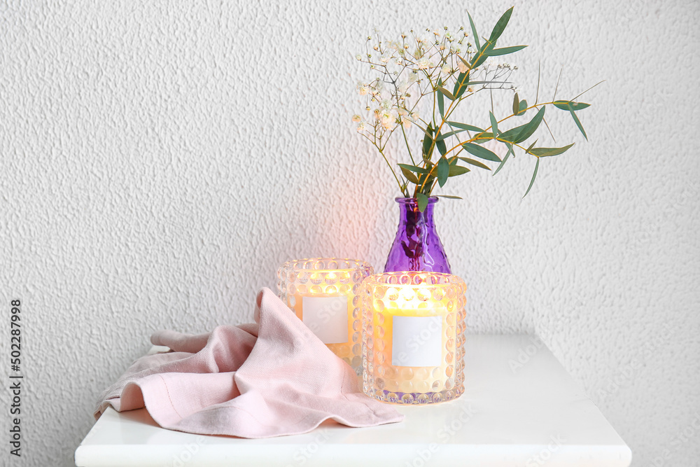 Burning candles in holders and vase with flowers on table in room