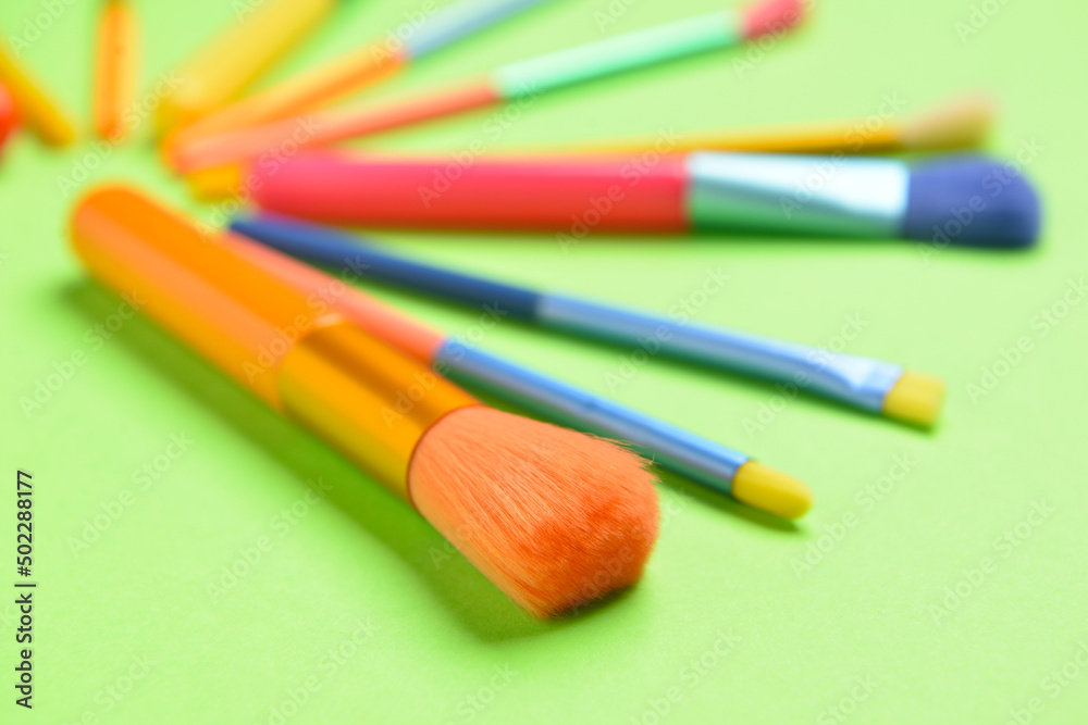 Set of colorful makeup brushes on green background, closeup
