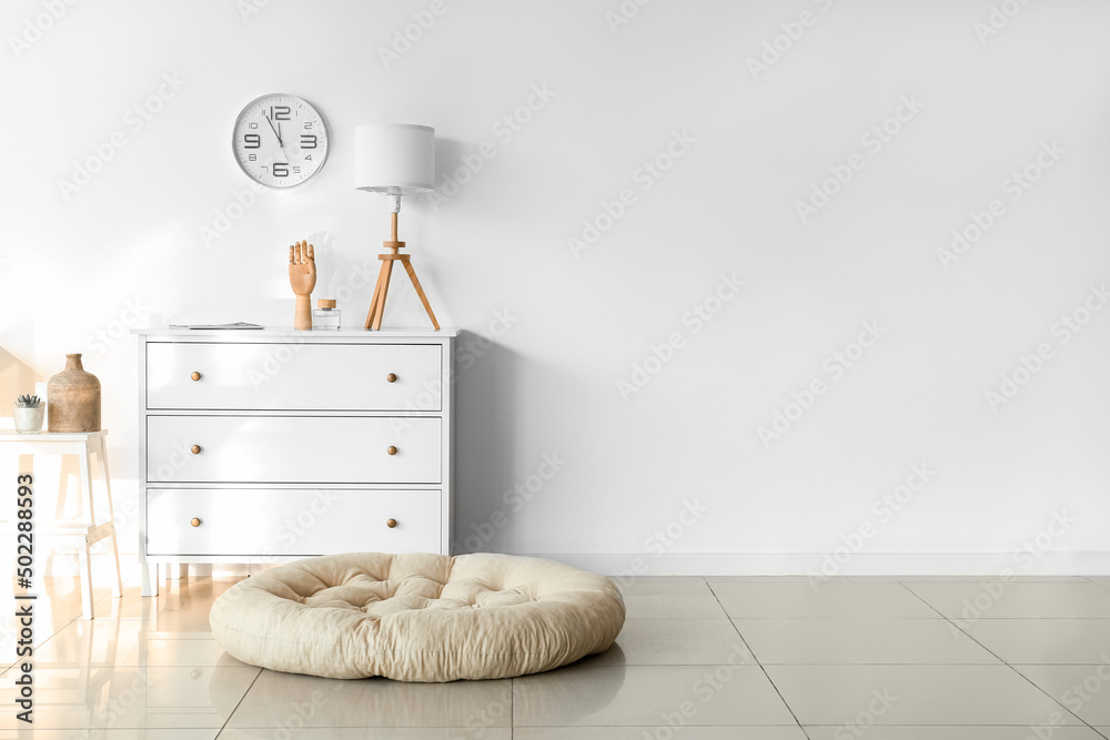 Chest of drawers with lamp, decor and clock hanging on light wall