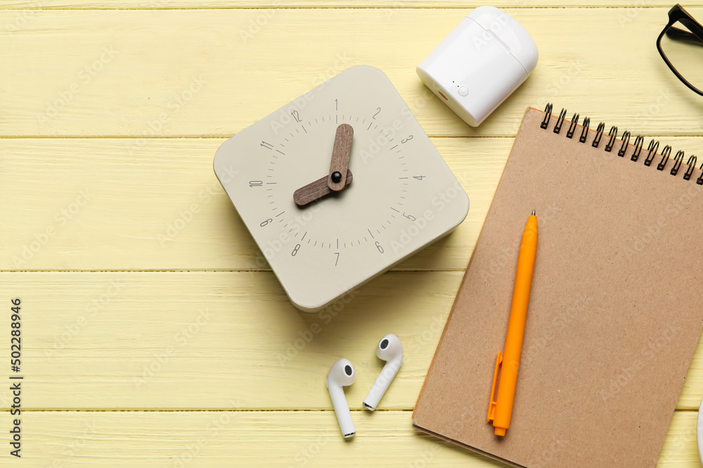 Alarm clock, notebook and earphones on color wooden background