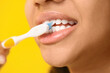 African-American teenage girl brushing teeth on yellow background, closeup