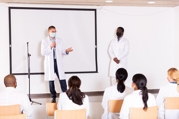 Canvas Print - Portrait of confident successful male coach in face mask for disease prevention giving speech at medical conference