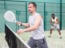 Young Adult Man Playing Paddle Tennis Doubles Match With Male Partner At Warm Sunny Day