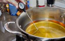 Chef checks the temperature of the heated oil in pot on gas stove with thermometer