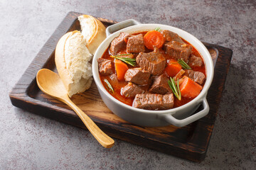 Wall Mural - Slowly stewed spicy beef in red wine with vegetables closeup in the wooden tray on the table. Horizontal