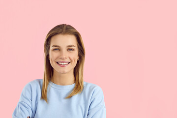 Wall Mural - Studio shot of beautiful young caucasian woman looking at camera with charming cute smile. Close up of blonde girl in light blue sweatshirt isolated on pink background. Banner. Isolated. Copy space.