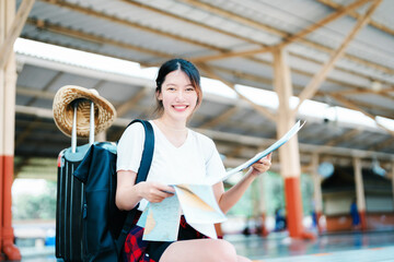 Wall Mural - summer, relax, vacation, travel, portrait of a cute Asian girl looking at a map to plan a trip while waiting at the train station.