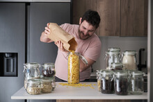 Young Latin Man Filling Up A Jar With Corn Flakes From A Paper Bag. Food In Bulk Delivery.