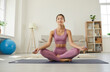 © Studio Romantic - Portrait of relaxed and calm happy young yogi woman meditating while exercising at home. Woman dressed in sportswear sits with her eyes closed on yoga mat in living room. Healthy lifestyle concept.