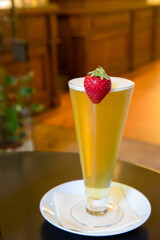 Poster - Vertical shot of a glass of a yellow cocktail decorated with a strawberry at a cafe